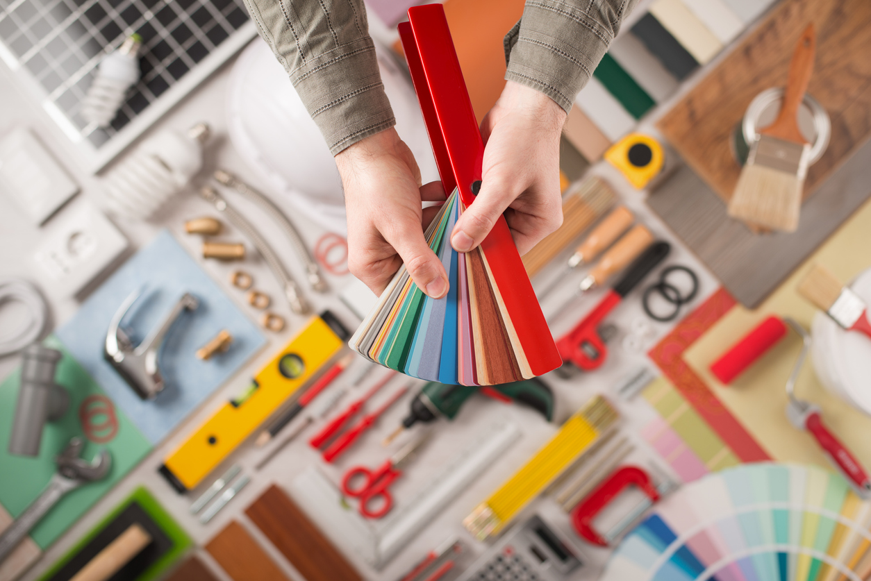 Hands holding material swatches over a table covered in remodeling tools.