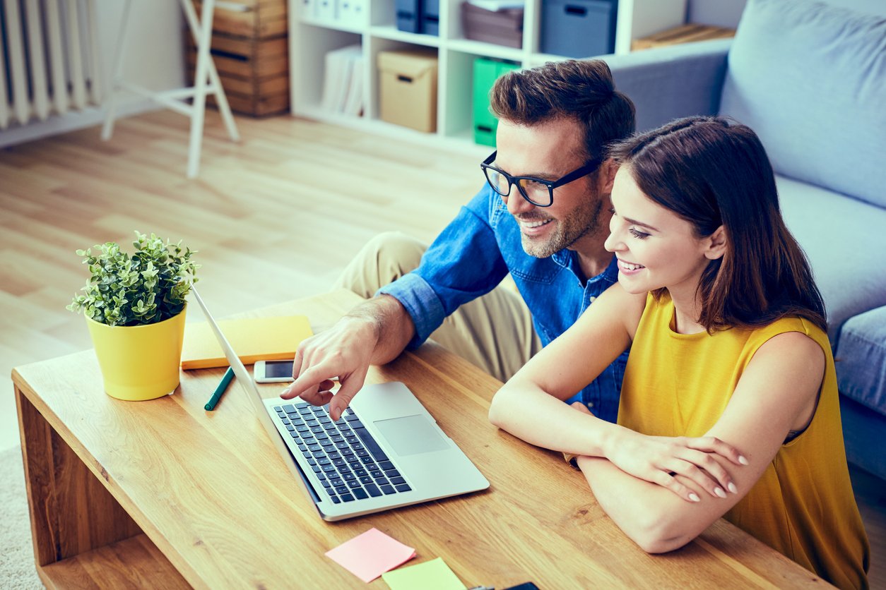 Happy couple using laptop togther; researching various home renovation costs and ideas.
